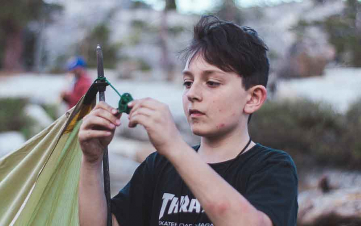 a young person works to tie a knot while setting up camp on an outward bound course